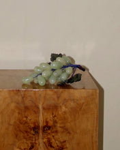 Load image into Gallery viewer, A decorative sculpture of light green grapes with dark green leaves and a blue stem, displayed on top of a polished wood block against a plain beige wall.
